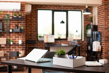 Organized, empty brick wall room with desk, chair, and digital devices for efficient research work at startup company. Clean workspace having a laptop, pot of plant and office materials on table.
