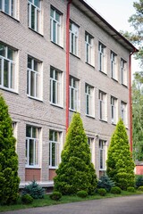 Exterior view of a school building featuring white windows, a red downspout, and green trees in the foreground