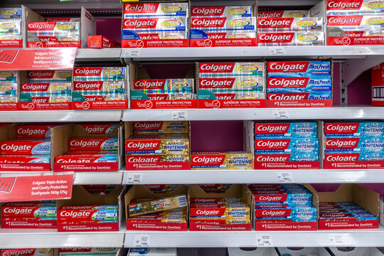 Multiple rows of Colgate toothpaste boxes are neatly stocked on retail shelves, priced for sale in an Australian supermarket.