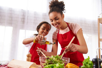 Small daughter pours olive oil into salad prepared by mother. Cooking and nutrition concepts.