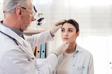 Obraz premium Doctor in white gown with stethoscope and female patient in office. Doctor is examining woman's head.