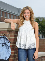 Beautiful young blonde female student on campus - standing next to backpack