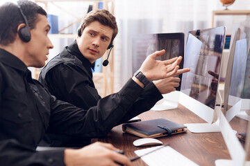 Two men work as guards. They sit in front of the monitors in the security room. The headphones are on their heads.