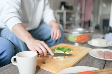 A Japanese pregnant woman in her 20s, wearing a dress that shows her stomach, sits on a sofa in her apartment and her husband cooks a hot pot dish.