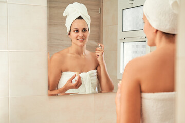 Woman applying perfume in bathroom mirror reflection. Skincare concept.