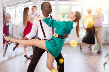 Gracious lady training tango in pair with man in dance-hall during dancing classes