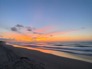 Obraz premium Golden Hour at the Coast: A picturesque panorama of a sandy beach meeting the vast ocean, painted in the golden hues of a breathtaking sunrise. The horizon is ablaze with colors, casting a soft.