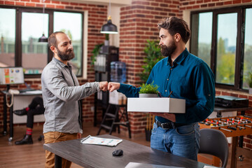 Fototapeta premium Male coworkers fist bumping in brick wall office, greeting each other, ready to work at startup company. Friendly interaction between businessmen in modern workspace, symbolizing teamwork and success.