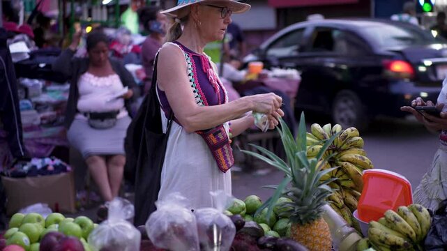 A mature woman paying for fresh fruits and vegetables in a lively outdoor market in Granada, Nicaragua, immersing herself in local culture.