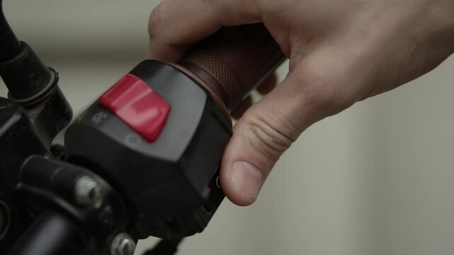 The biker has no gloves on his hands, he takes the handlebars of the motorcycle with his right hand, presses the kill switch and presses the starter button to start the motorcycle, turns the throttle