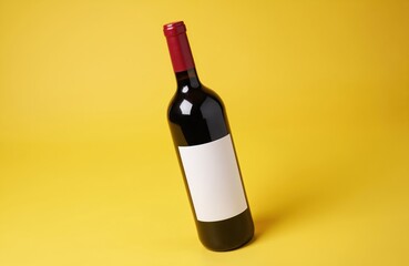 Red wine bottle with blank label stands against yellow background. Studio shot offers excellent copy space for branding. Product presentation for design branding ideas. Bottle ideal for wine drink