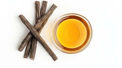 Top view of licorice roots and a bowl of golden licorice tea on a white background.