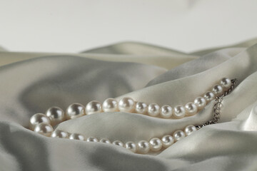 Beautiful pearl necklace on white silk, closeup