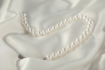 Beautiful pearl necklace on white silk, closeup