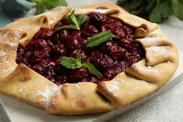 Tasty galette with cherries and mint on light table, closeup