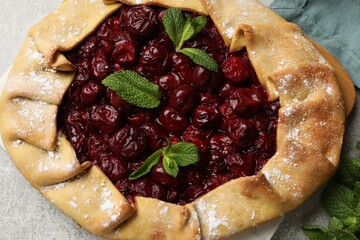 Tasty galette with cherries and mint on light table, top view