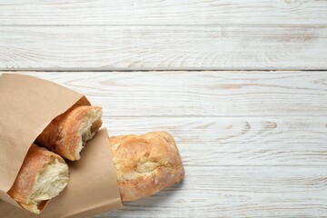 Paper bags with fresh baguettes on wooden table, top view. Space for text