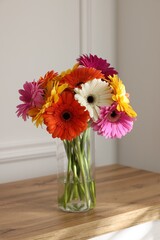 Bouquet of beautiful gerbera flowers in glass vase on wooden table indoors