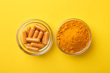Turmeric powder and capsules on yellow background, top view