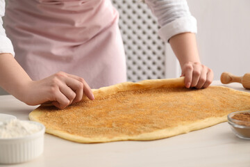 Making cinnamon rolls. Woman shaping dough at white table, closeup