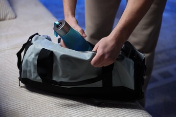 Man putting bottle of water into gym bag indoors, closeup