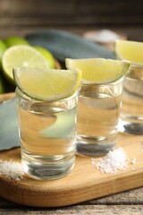 Tequila shots with lime slices, salt and agave leaves on wooden table, closeup