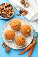 Tasty carrot muffins, walnuts and fresh vegetables on light blue wooden table, flat lay