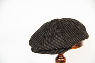 Concept photo of a newsboy cap made of black herringbone wool fabric mounted on a bronze mannequin head. Product catalog photo of a classic newsboy cap isolated on a white background