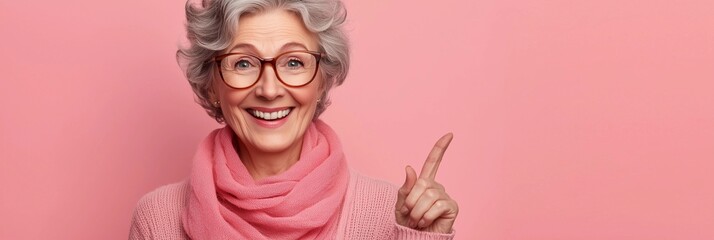 Fototapeta premium Smiling elderly woman with gray hair and glasses gestures positively against a pink background