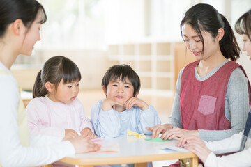 折り紙を折る保育士と園児