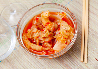 Portion of kimchi served in glass bowl with chopsticks. Korean side dish.