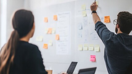 Two professionals collaborate on a strategy using sticky notes on a white board during business meeting