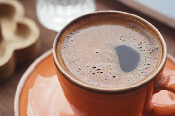 Warm coffee in an orange cup on a rustic wooden table