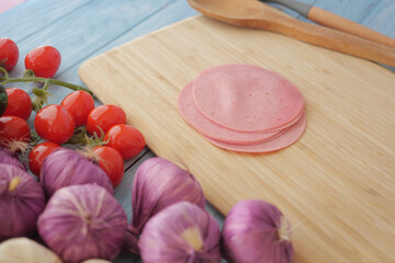 Sliced deli meat with tomatoes and garlic on a wooden cutting board