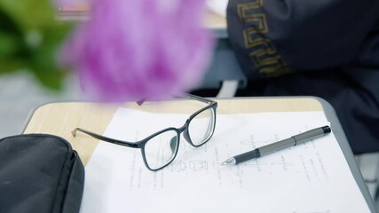 School desk scene with eyeglasses, test papers, and writing pen during study session