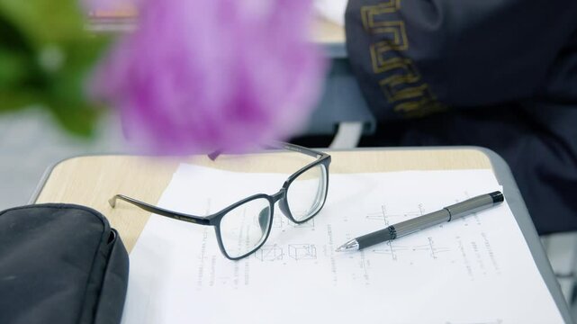 School desk scene with eyeglasses, test papers, and writing pen during study session