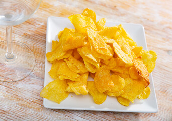 Potato chips in square ceramic plate on rustic wooden table. Top view. Close up