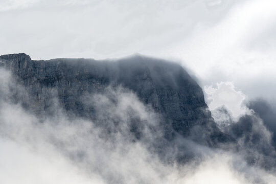 Large rocky mountain with mist and clouds and areas of transparent sky
