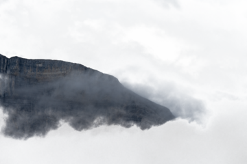 Rocky bluish mountain surrounded by partially transparent clouds and mist

