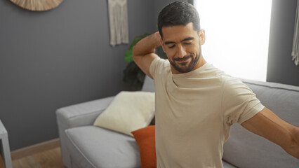 Fototapeta premium Young man stretching indoors in a cozy living room with modern decor and natural light, showcasing a relaxed and comfortable home environment.