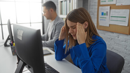 Woman stressed in office with man working at computer in background showcasing business environment...
