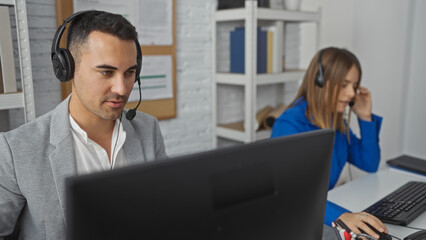Man and woman with headsets working in an office at computers, representing collaboration in a...