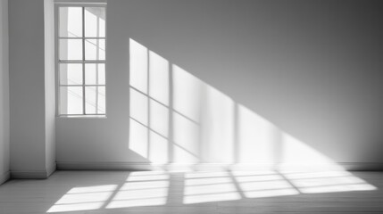 Fototapeta premium Sunlight streams through window in empty room, casting shadows on white wall and floor; ideal for minimalist design