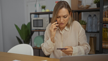 Woman talking on phone while holding credit card at office, looking concerned with expressions in indoor workspace environment.