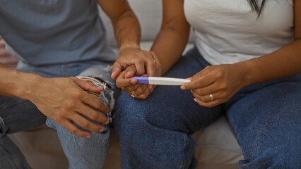 Couple sitting on a couch indoors holding a pregnancy test together, capturing a moment of anticipation and emotion in a home environment