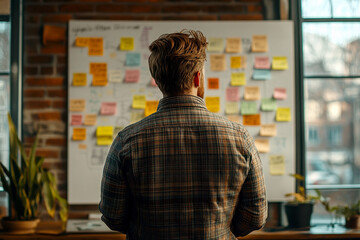 a man look to sticky notes on a task board to organize ideas and workflow in a office.