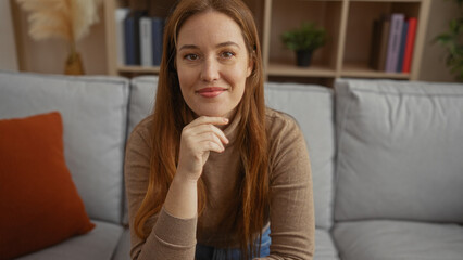 Woman sitting in cozy living room at home with thoughtful expression featuring books and plant in...