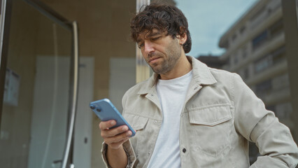 Young man standing in an urban street using smartphone with focused expression reflecting modern digital lifestyle in a vibrant city setting.