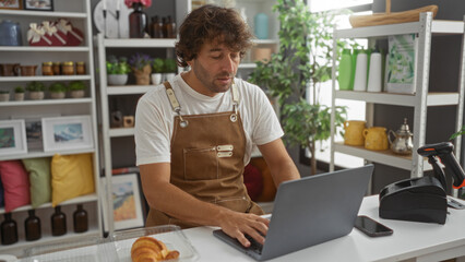 Fototapeta premium Young man working on laptop in home decor store with various decorations and plants in the background