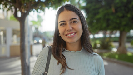 Woman smiling in a sunlit urban park setting, showcasing a youthful and attractive appearance with...